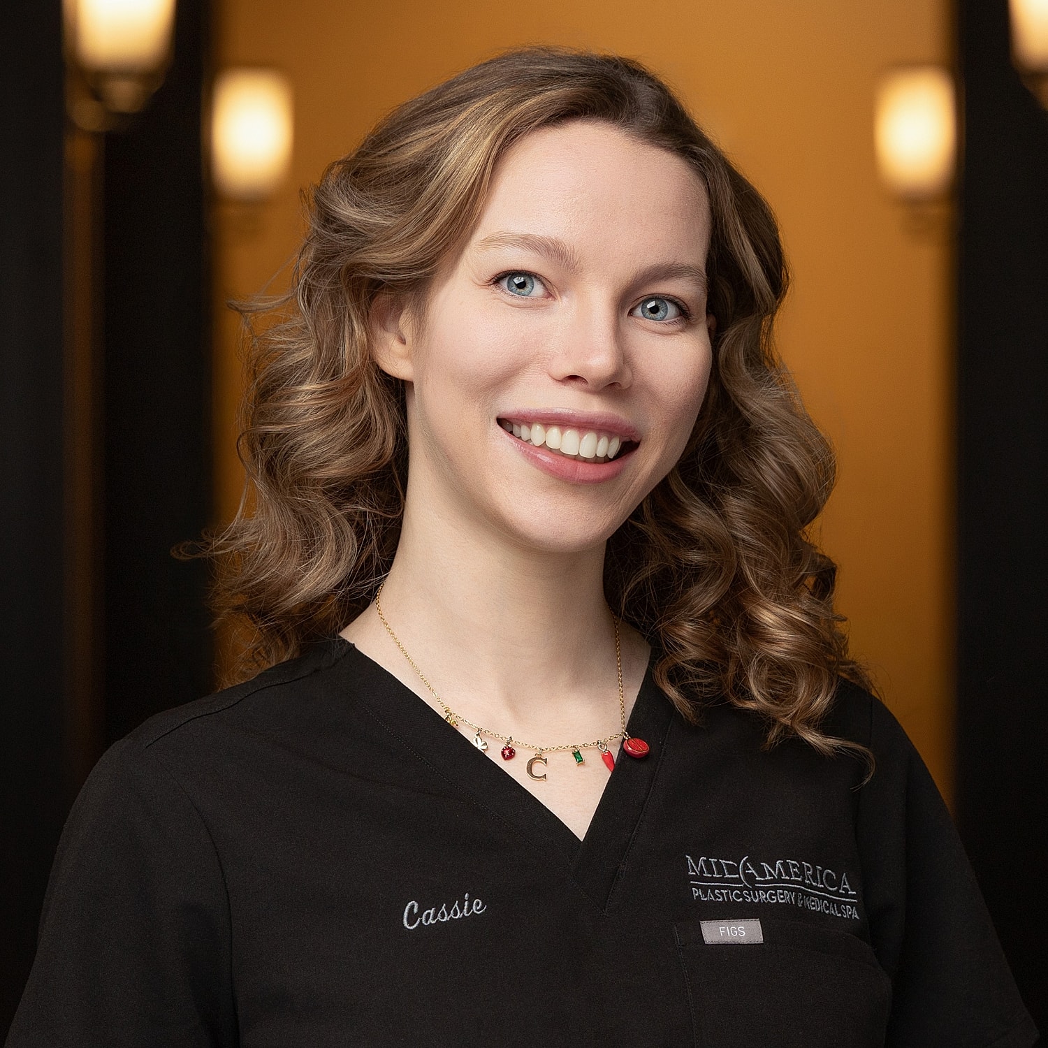 Smiling woman in medical attire with curly hair.
