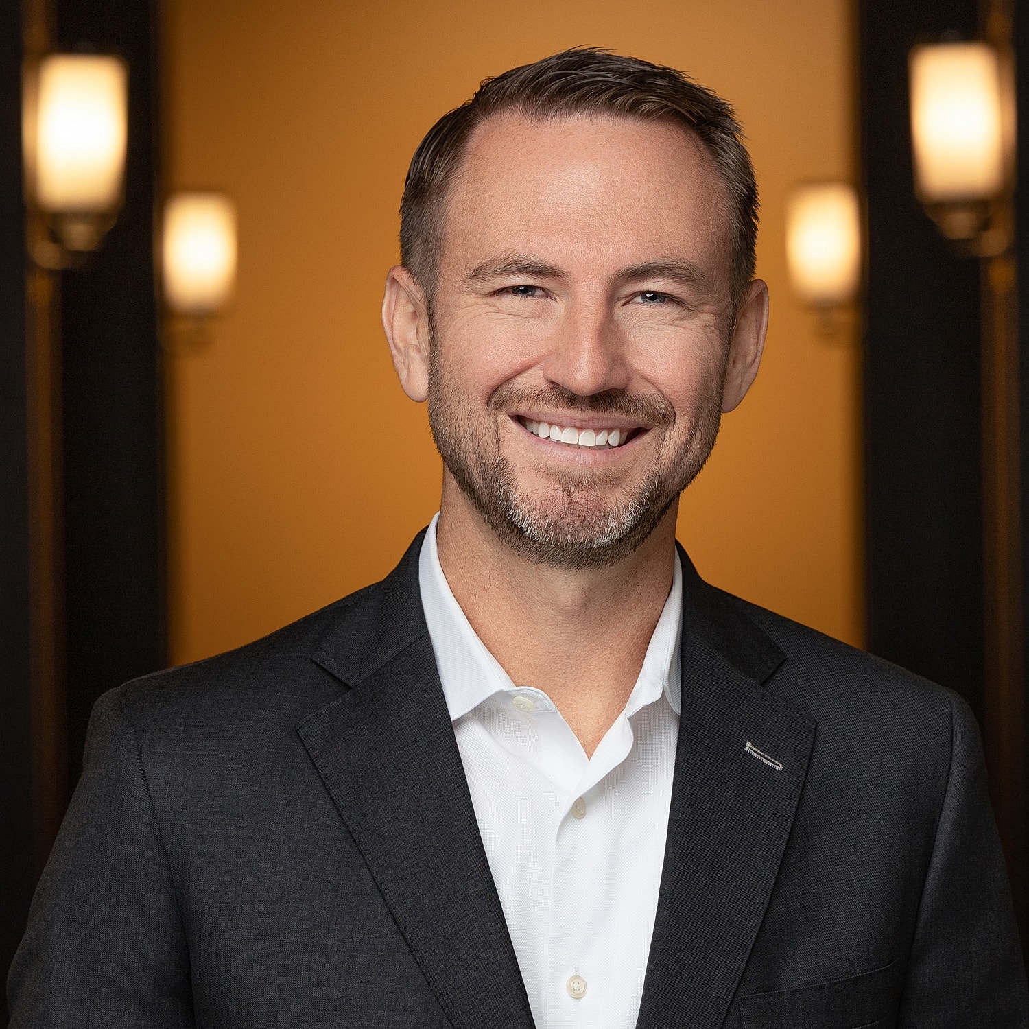 Smiling man in suit against warm background.