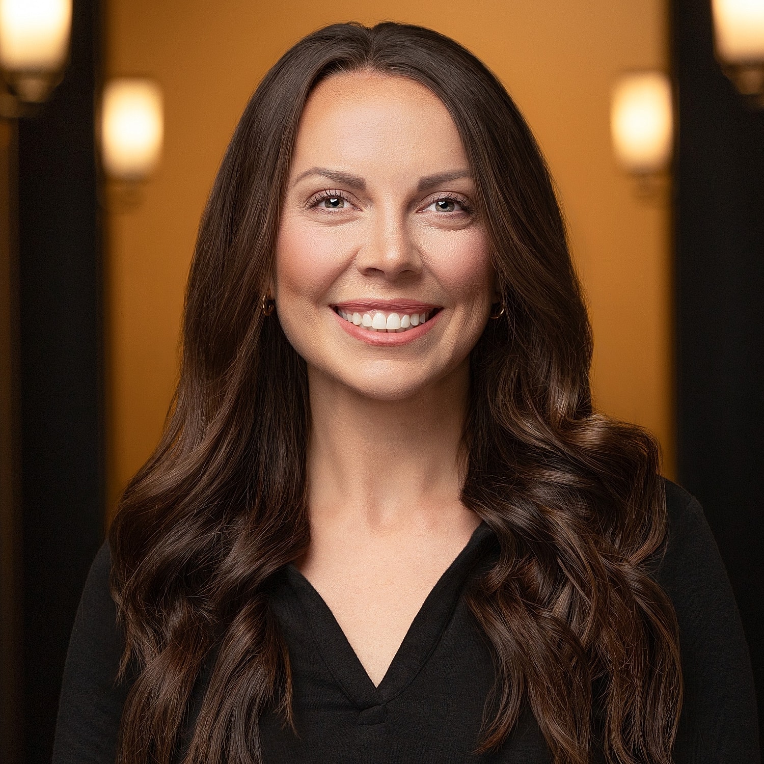 Smiling woman with long dark hair, warm background.