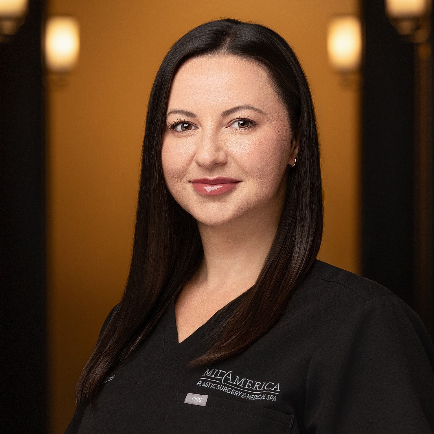Medical professional in black scrubs, smiling portrait.
