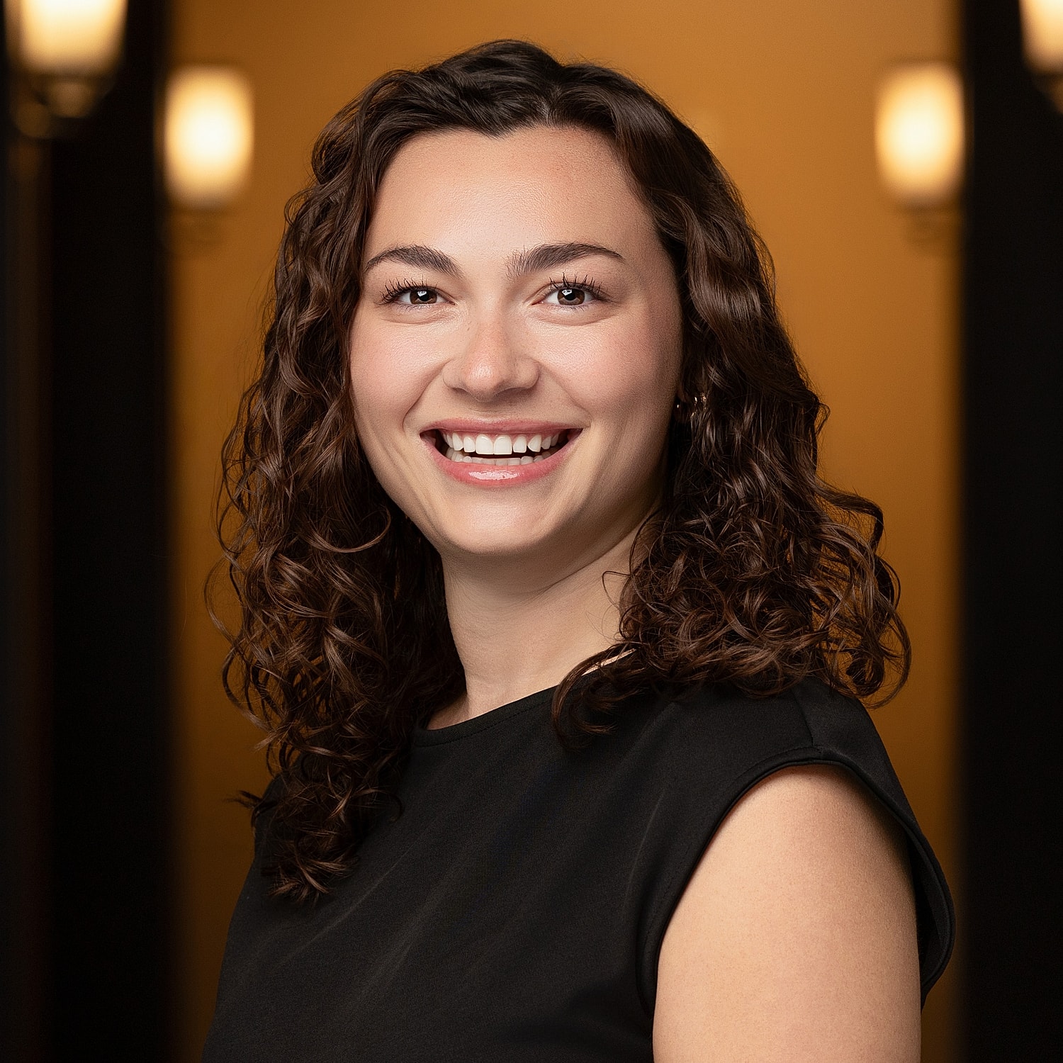 Smiling woman with curly hair in black top.